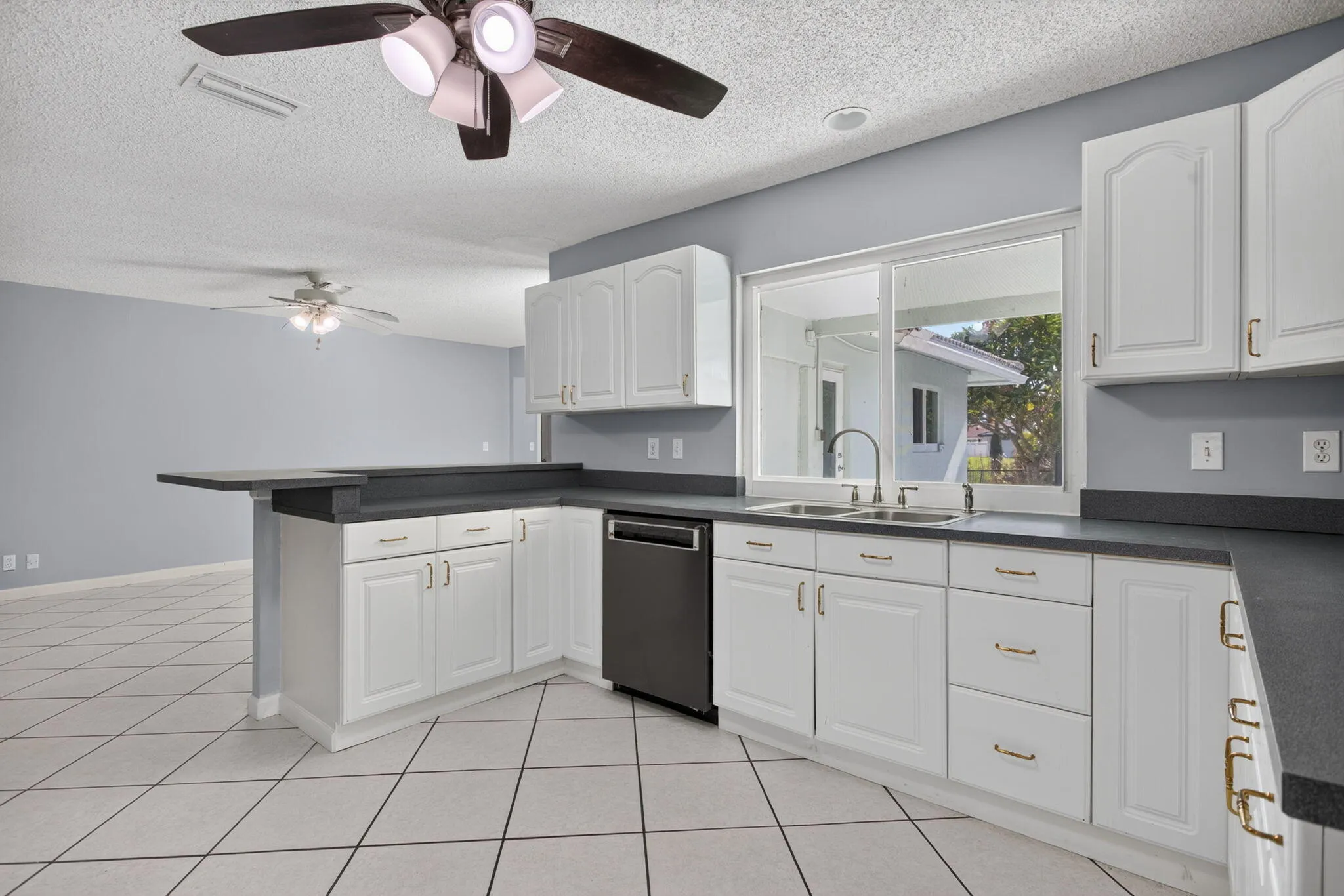 Kitchen featuring white cabinetry, dark countertops, tile flooring, a dual-basin sink with a gooseneck faucet, and a built-in dishwasher