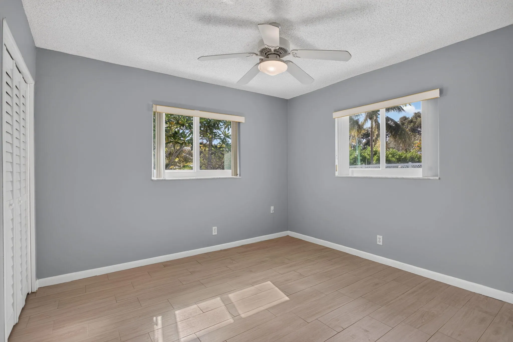 Wood-finish flooring, ceiling fan with integrated lighting, louvered closet doors, and multiple windows