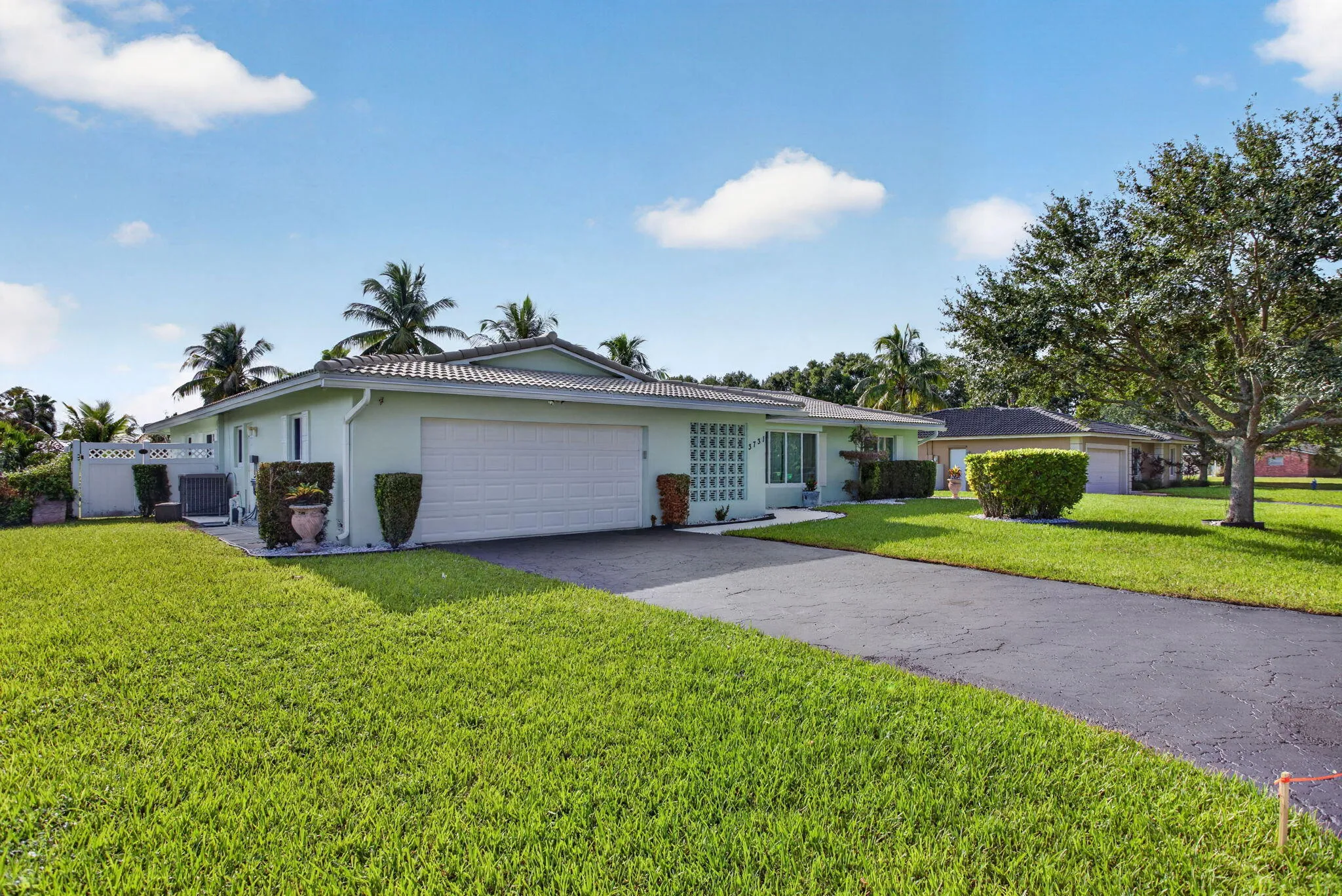 Light green exterior with a two-car garage, gray tile roof, paved driveway, and established landscaping