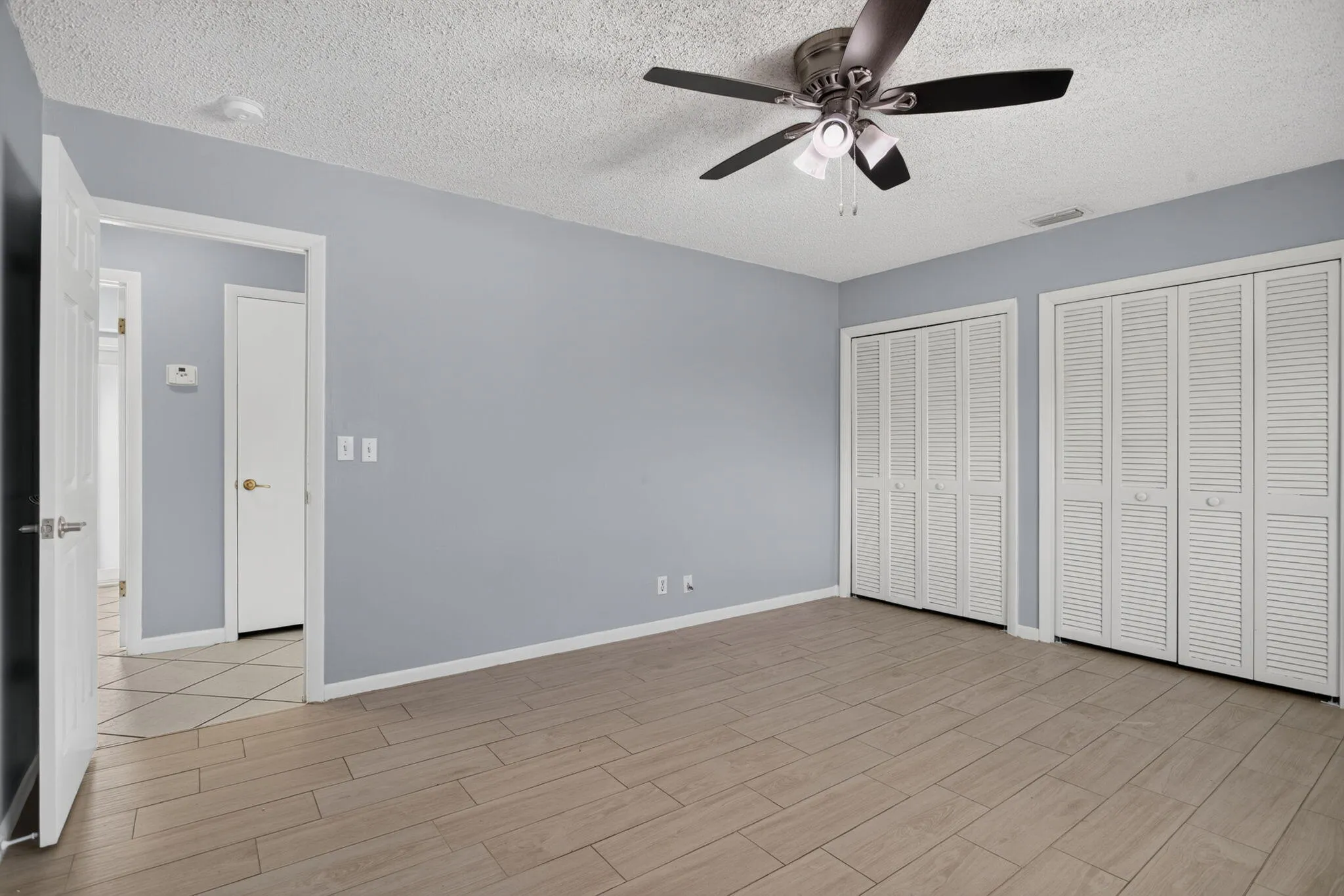 Wood-finish flooring, ceiling fan with integrated lighting, two bi-fold louvered closet doors, and light blue wall paint