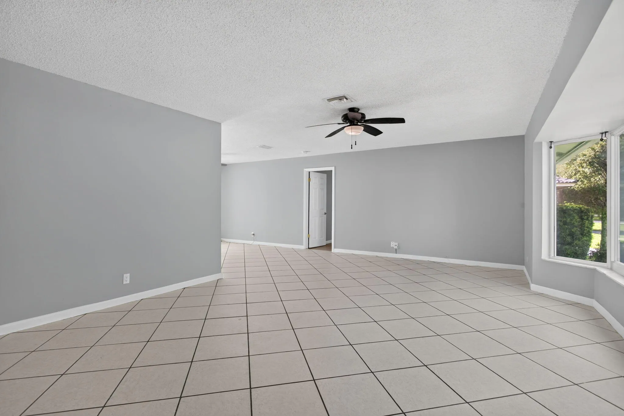 Tile flooring throughout, neutral gray wall tones, ceiling fan, and a wide bay window