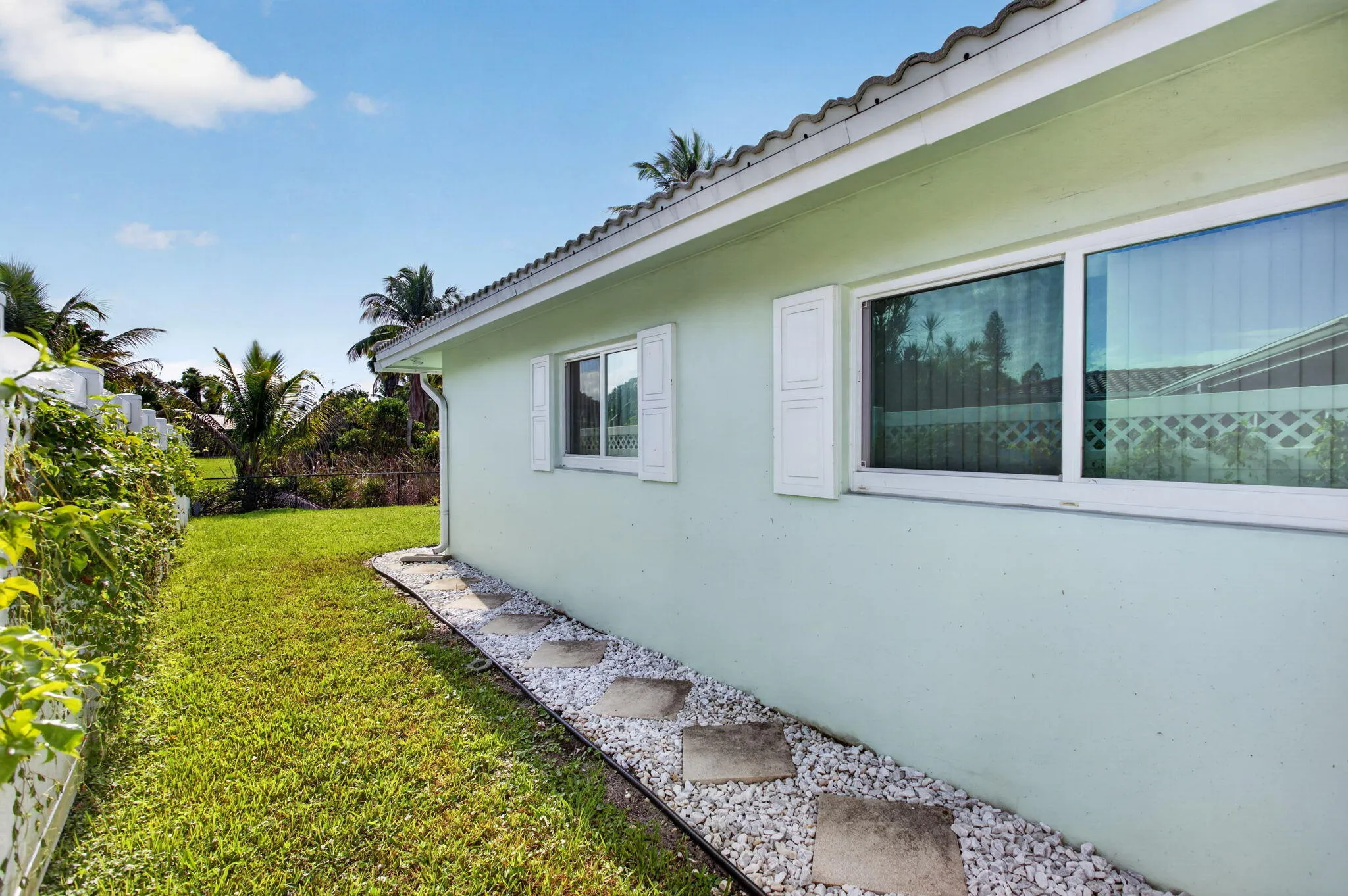 Exterior featuring a stucco finish, multiple windows with white frames, decorative white shutters, and a white gravel pathway with stepping stones