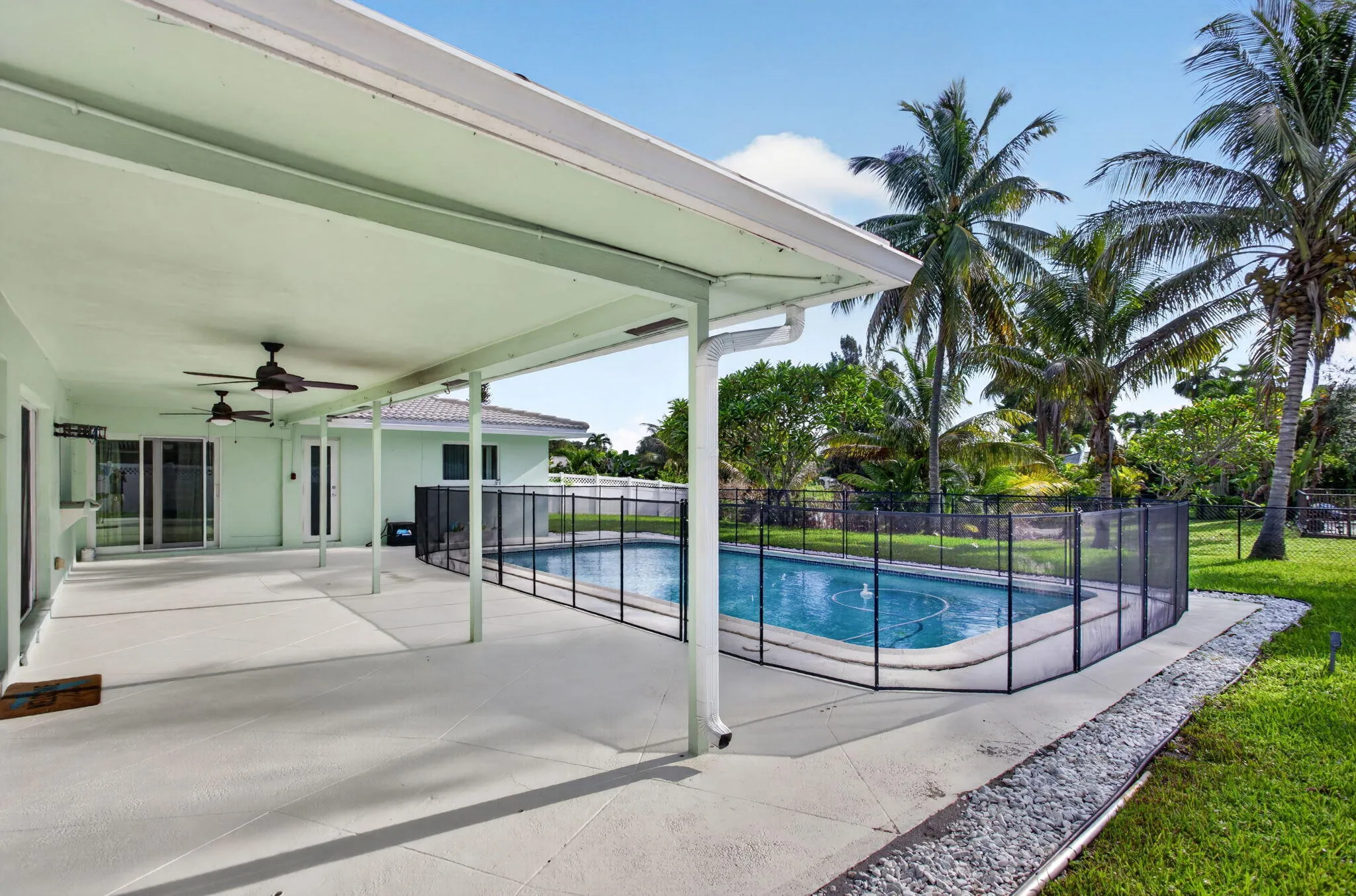 Expansive covered patio with multiple ceiling fans, overlooking a fenced swimming pool