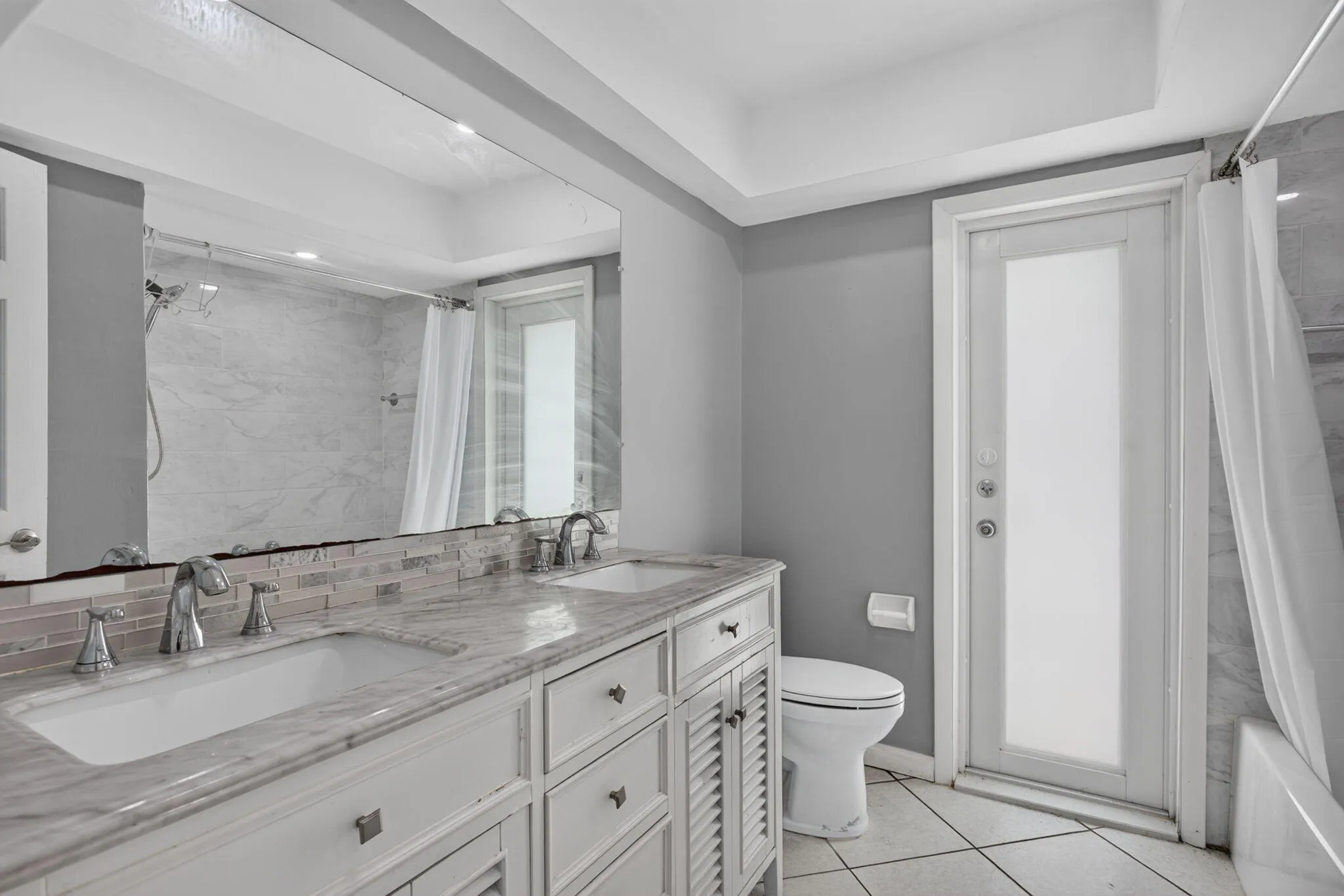 Dual vanity with integrated sinks, patterned tile backsplash, polished chrome fixtures, and a large wall-mounted mirror