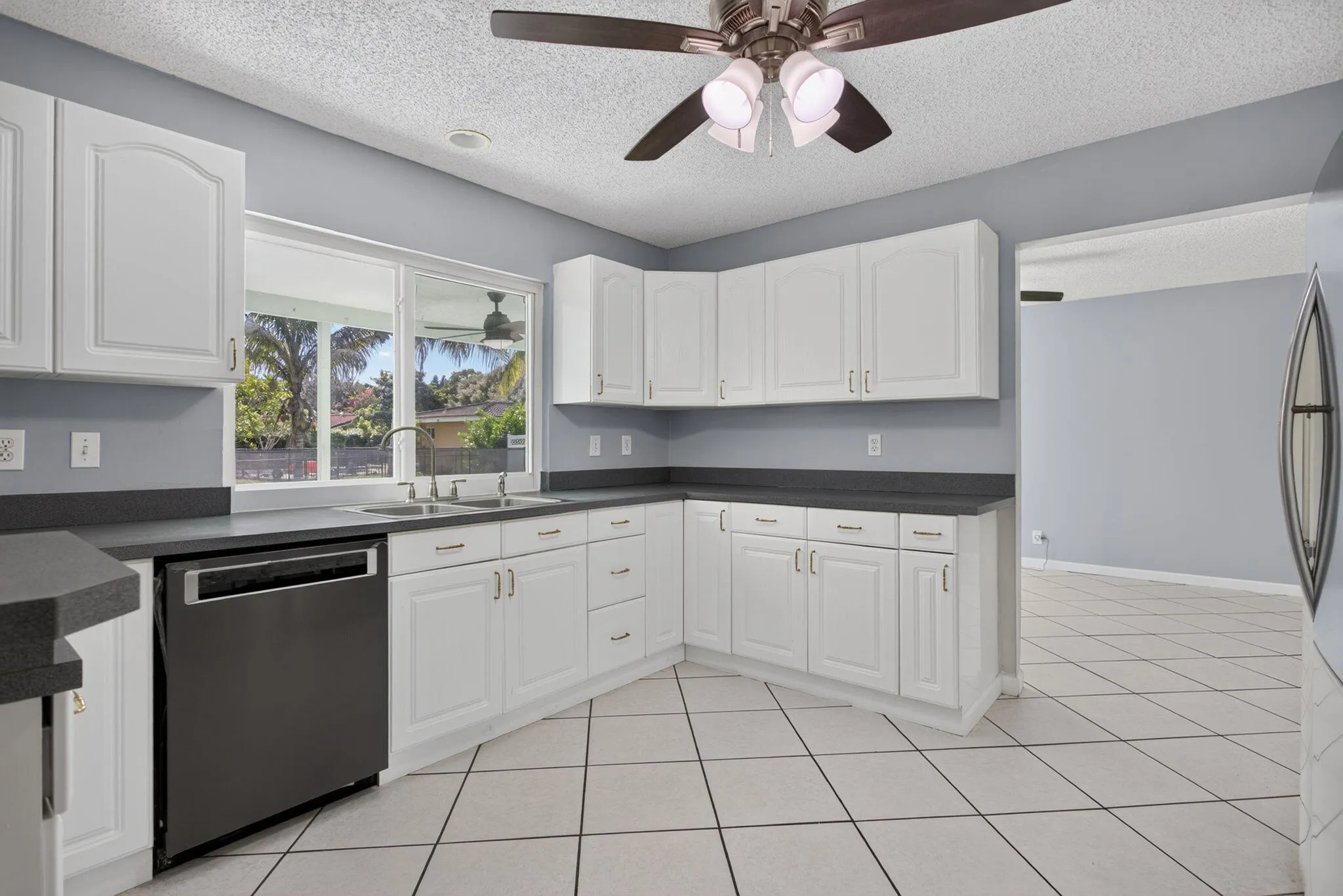 Kitchen featuring white cabinetry, dark countertops, tile flooring, a stainless steel sink, and a modern ceiling fan