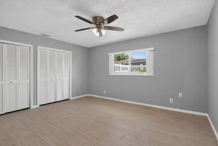 Wood-finish flooring, louvered bi-fold closet doors, ceiling fan with integrated lighting, and a single window