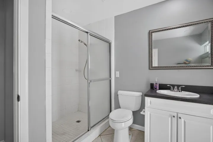 Shower enclosure with clear glass and frosted panels, white tile surround, and a white vanity with a dark countertop and undermount sink
