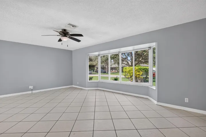 Spacious room featuring neutral tone tile flooring, a multi-pane bay window, and a ceiling fan with integrated lighting