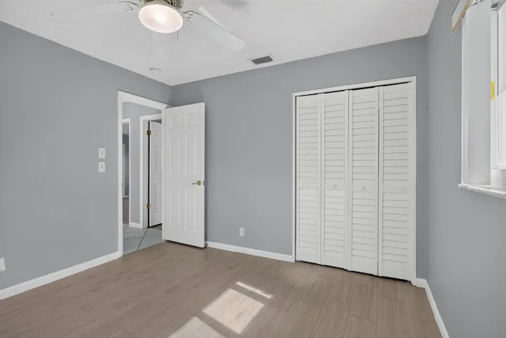 Wood-finish flooring, ceiling fan with integrated lighting, louvered bi-fold closet doors, and light gray wall finish