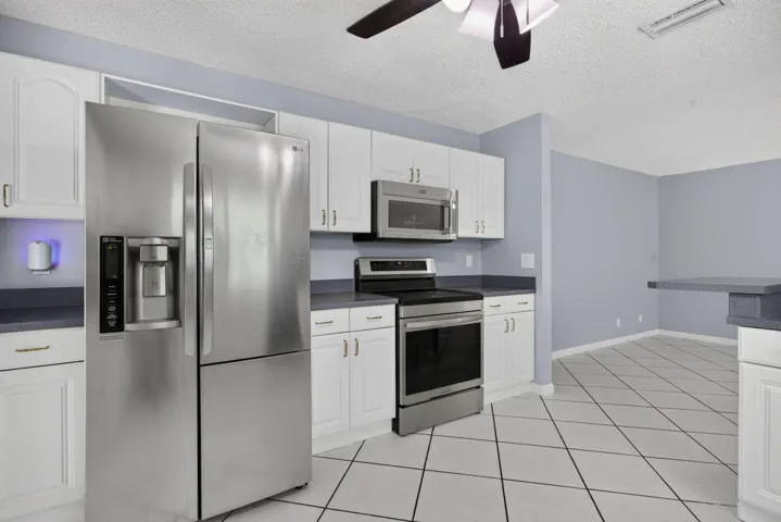 White cabinetry, stainless steel appliances, dark countertops, tiled flooring, and a ceiling fan