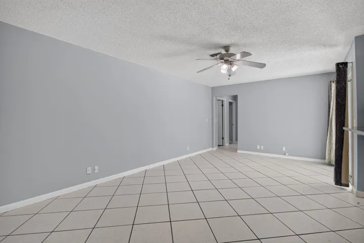 Expansive room featuring light gray walls, square tile flooring, and a ceiling fan with integrated lighting