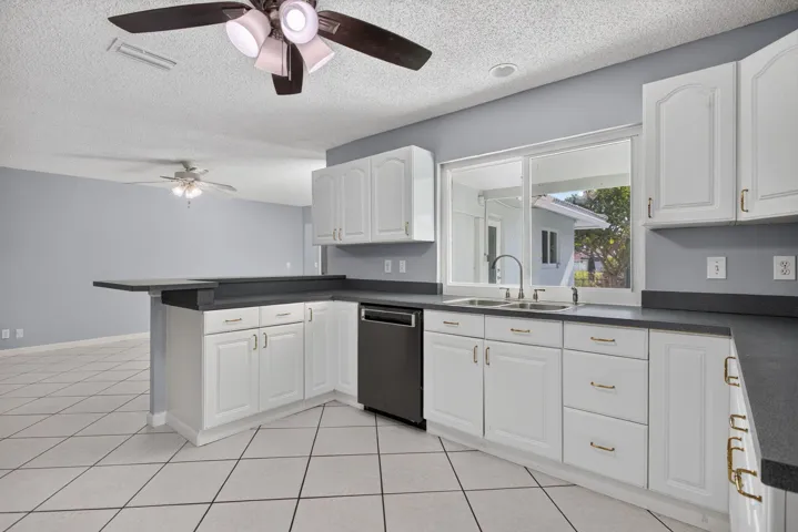 Kitchen featuring white cabinetry, dark countertops, tile flooring, a dual-basin sink with a gooseneck faucet, and a built-in dishwasher