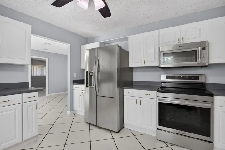 Kitchen featuring white cabinetry, dark countertops, stainless steel appliances, and diagonal tile flooring