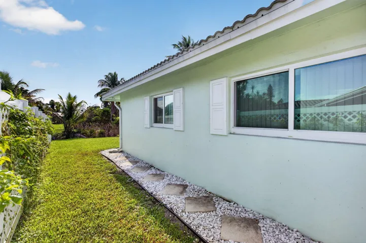 Exterior featuring a stucco finish, multiple windows with white frames, decorative white shutters, and a white gravel pathway with stepping stones