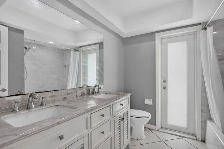 Dual vanity with integrated sinks, patterned tile backsplash, polished chrome fixtures, and a large wall-mounted mirror