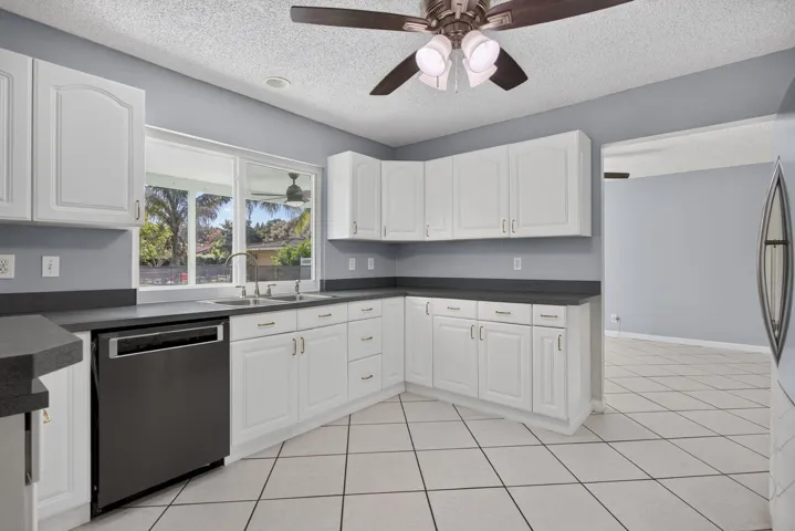 Kitchen featuring white cabinetry, dark countertops, tile flooring, a stainless steel sink, and a modern ceiling fan