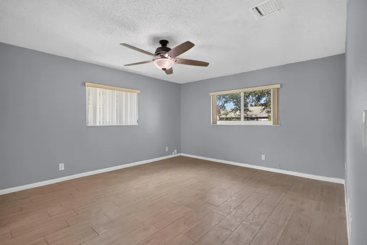 Wood-finish plank flooring with light gray walls, two windows, and a ceiling fan with integrated lighting