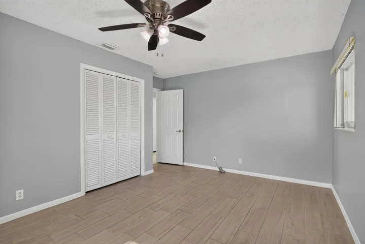 Light wood-finish flooring, louvered bi-fold closet doors, ceiling fan with integrated lighting, and a white interior door