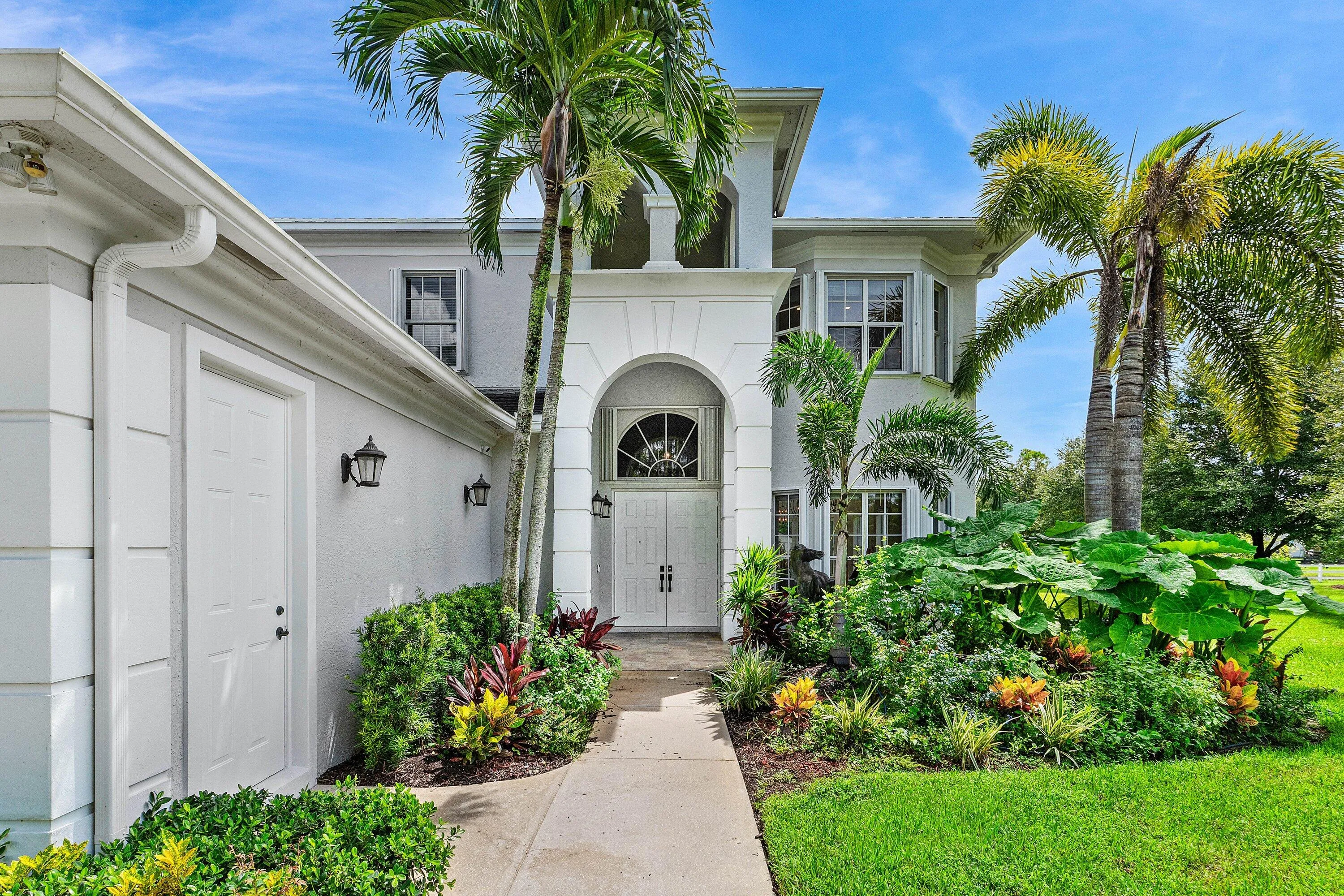 Arched Entryway featuring double doors, lush landscaping, and mature palm trees
