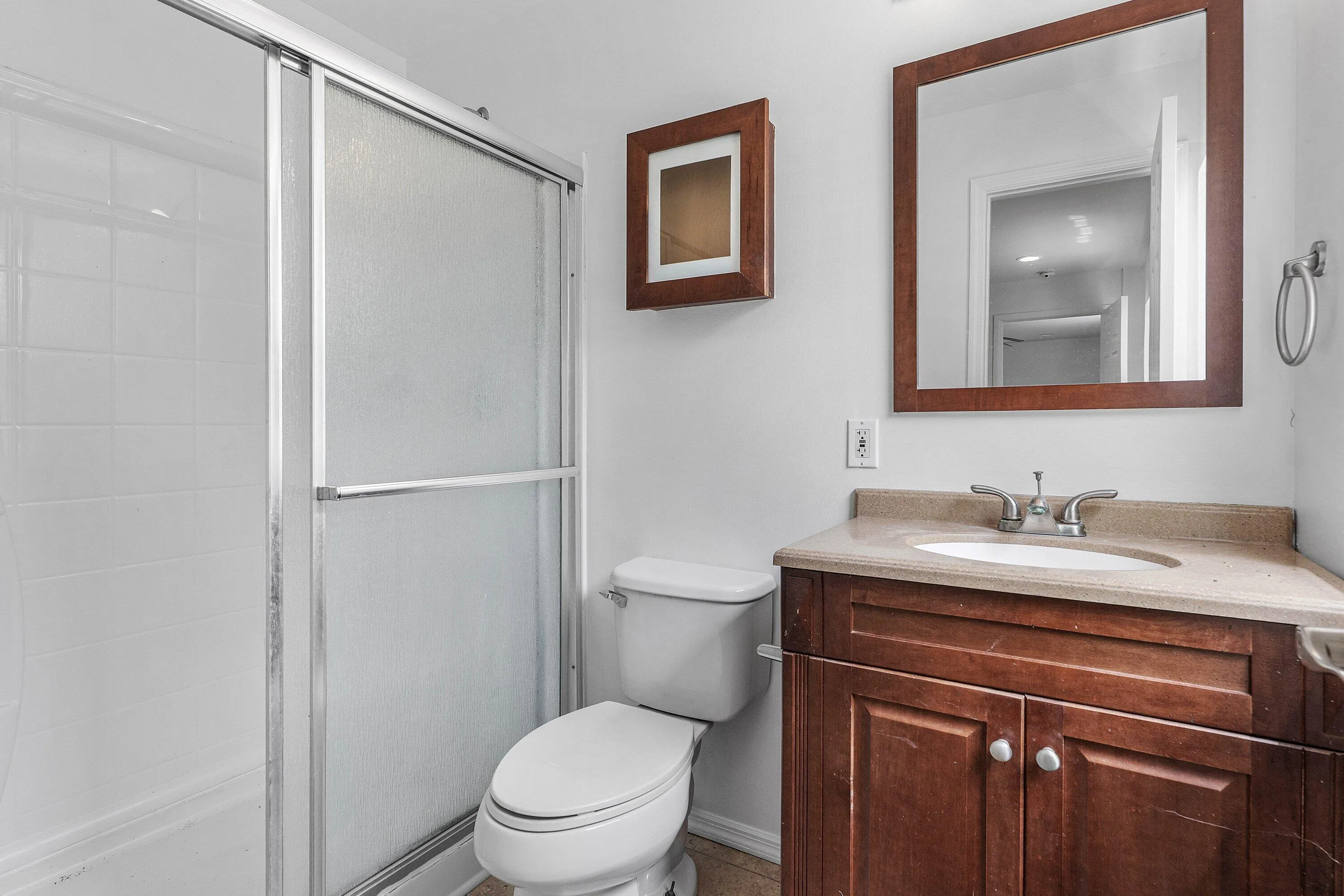Bathroom featuring a shower with sliding glass doors, white tiled walls, a wood-finish vanity with a built-in sink, and a framed mirror