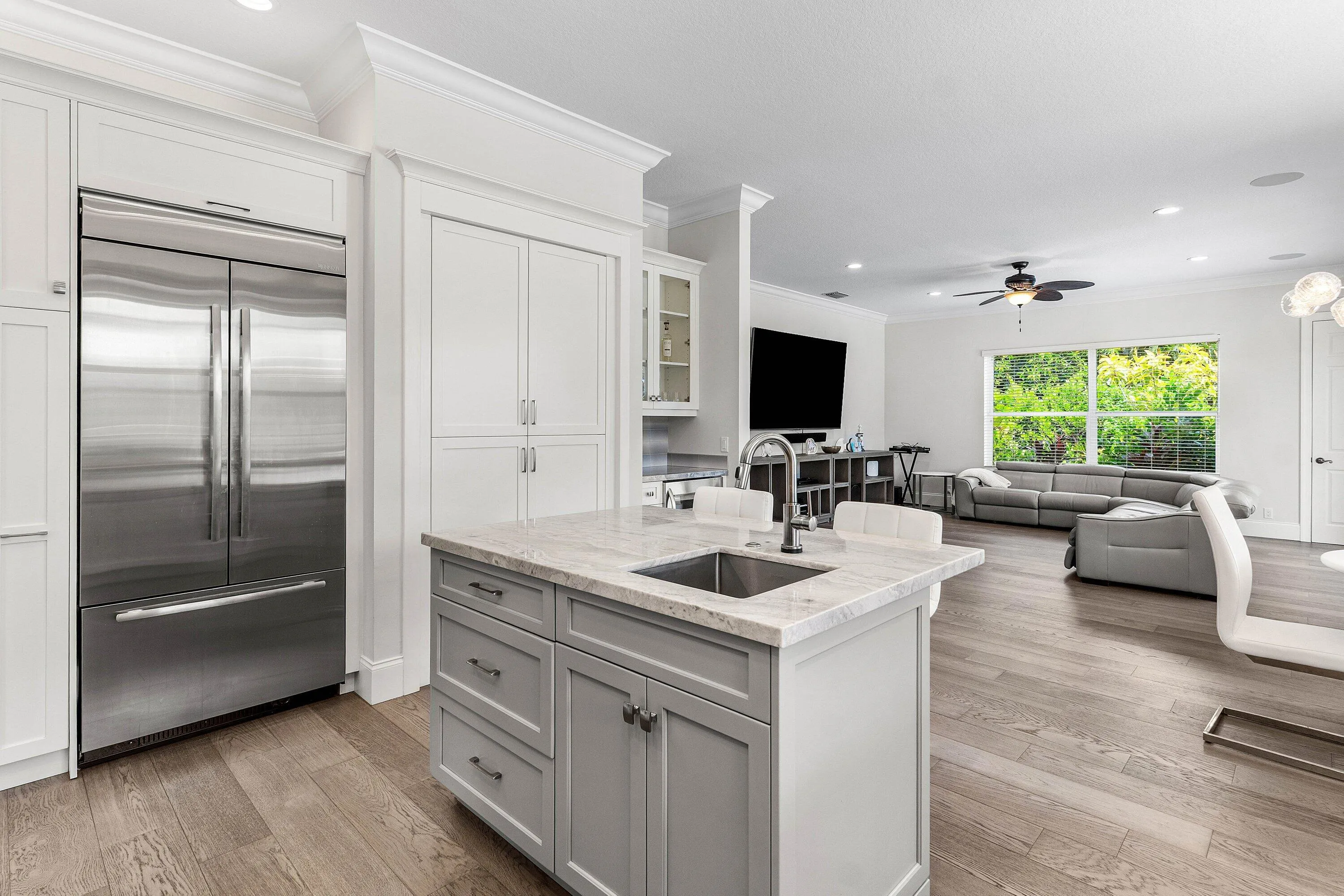 Wood-finish flooring throughout, kitchen with white upper and gray lower cabinetry, stainless steel appliances, recessed lighting, and a contemporary chandelier
