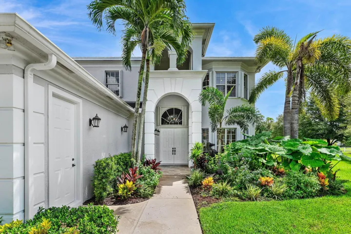Arched Entryway featuring double doors, lush landscaping, and mature palm trees
