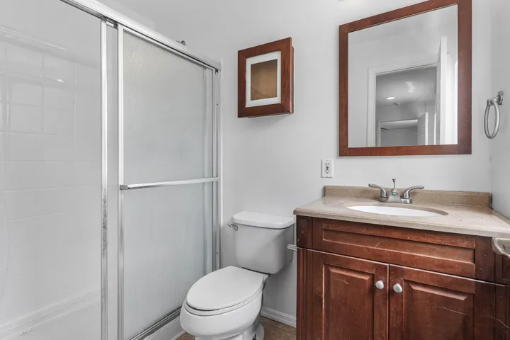 Bathroom featuring a shower with sliding glass doors, white tiled walls, a wood-finish vanity with a built-in sink, and a framed mirror