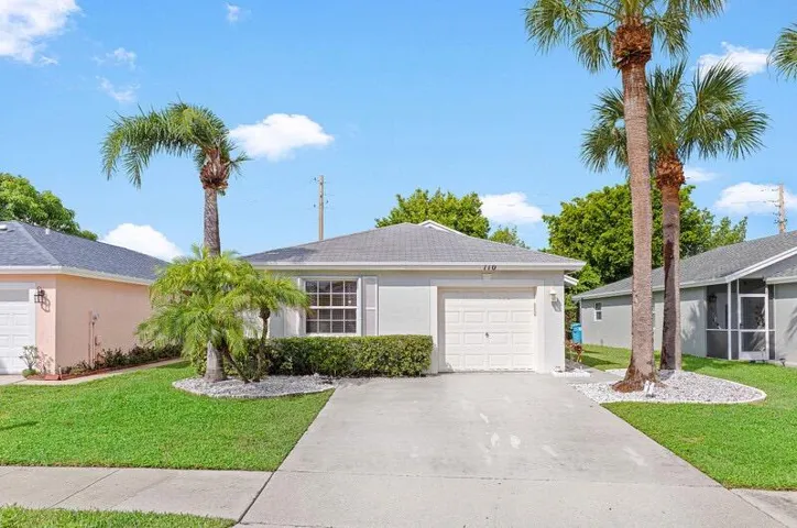 Concrete driveway, attached garage, well-maintained lawn, mature palm trees, and low-profile landscaping