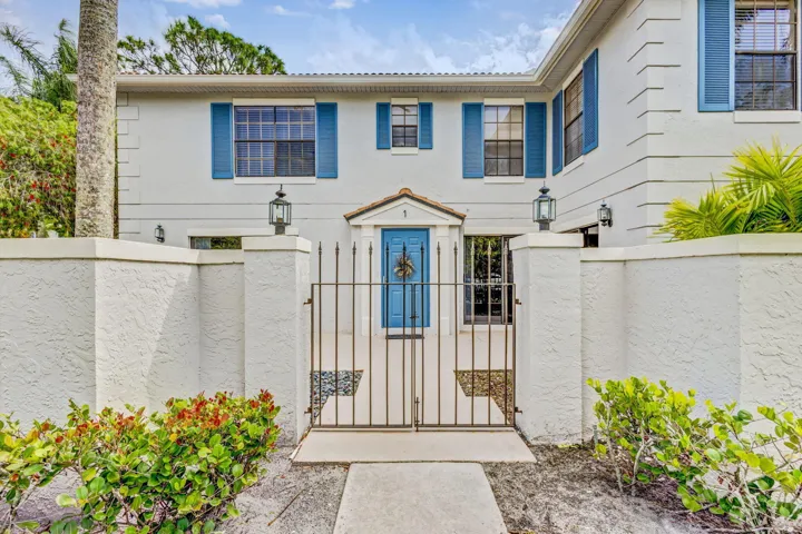 Stucco exterior with blue window shutters, an arched entryway, a privacy wall, a metal entry gate, and decorative exterior lighting