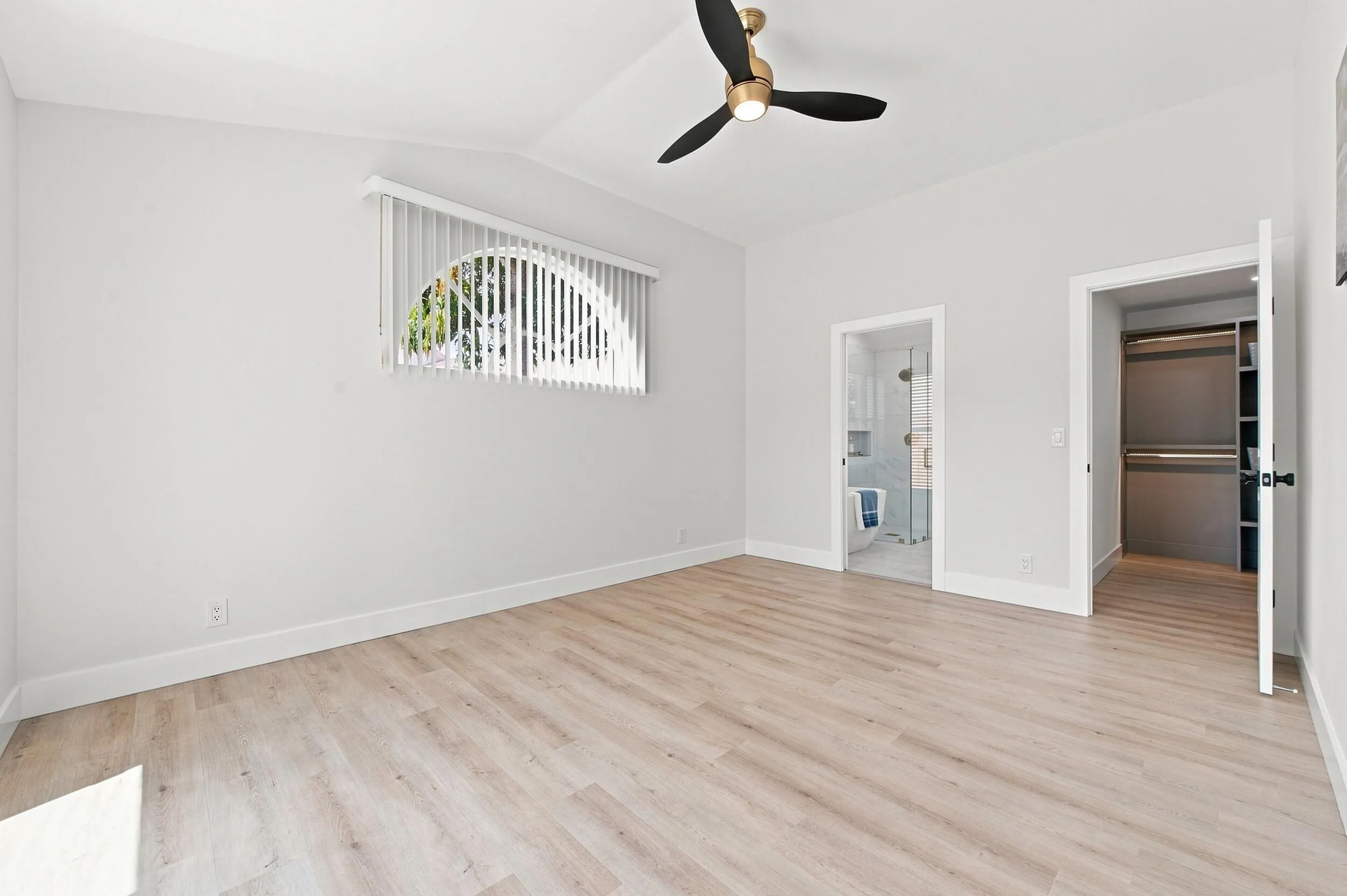 Vaulted ceiling with a brass-finish ceiling fan, wood-finish flooring, and white wall finishes