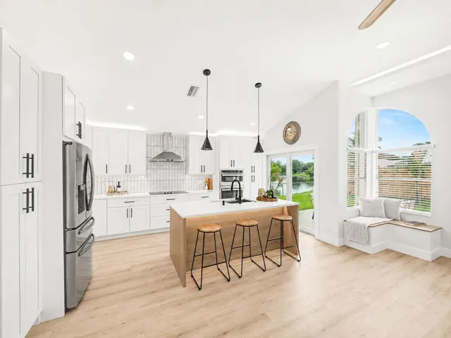 Modern kitchen featuring white cabinetry, stainless steel appliances, a center island with countertop seating, wood-finish flooring, and a built-in window bench
