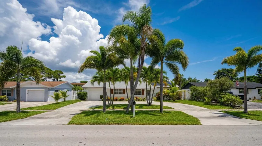 Curb appeal with mature palm trees, a well-maintained lawn, and a light-toned exterior