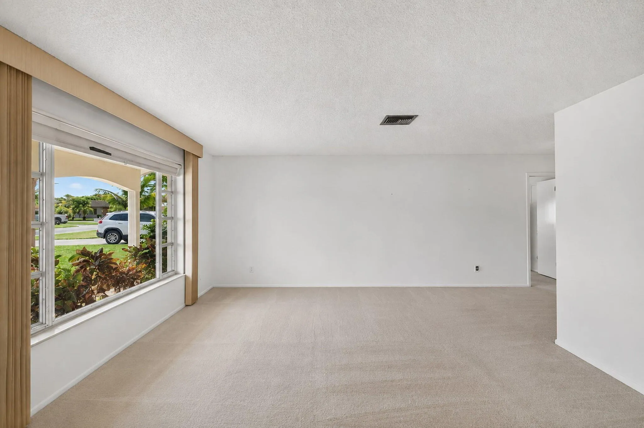 Expansive room with neutral carpeting and a large front-facing window