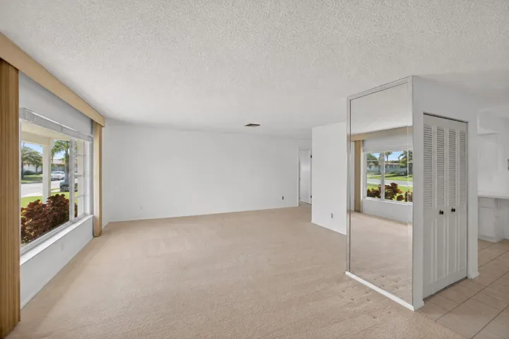 Neutral carpet flooring, white painted walls, large window with outdoor landscaping, mirrored wall accent, louvered bi-fold closet doors