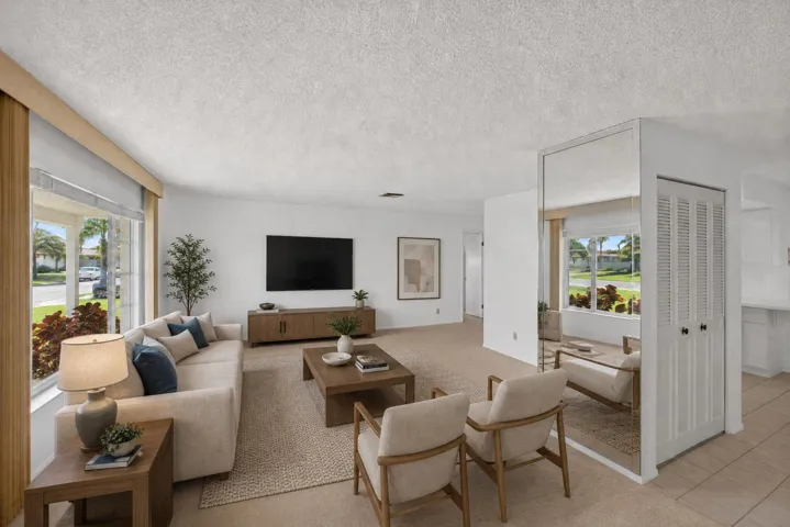 Expansive living area featuring large windows, neutral carpeting, and a mirrored accent wall