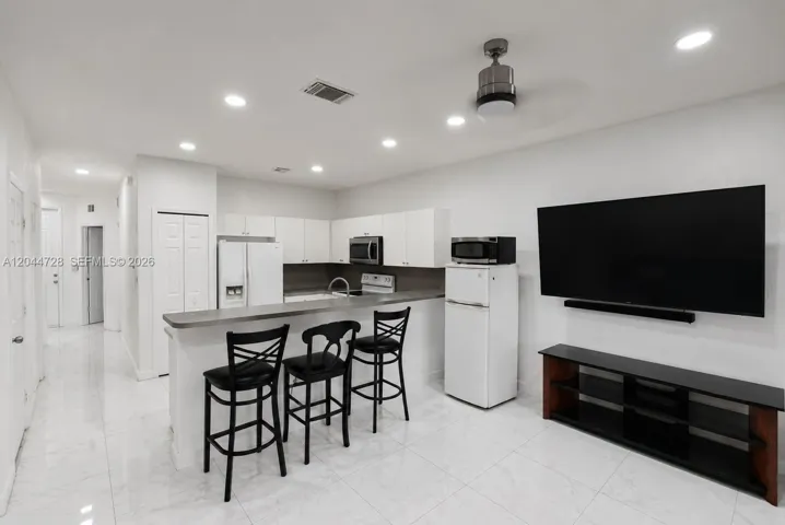 Bright open kitchen and living area with white appliances, and clean tile flooring. Clean, functional layout with a contemporary feel.