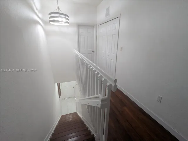Clean hallway with white walls, laminated flooring, and modern light fixture. Features a sleek staircase and multiple doors for convenient access.