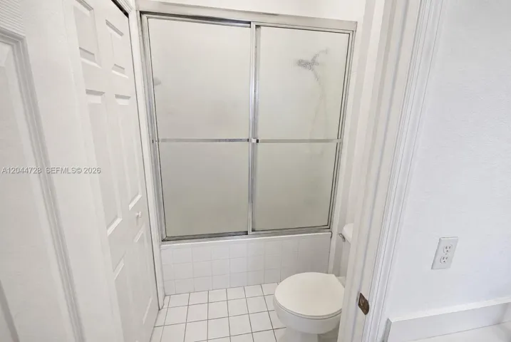 1st Master Bathroom with white tile flooring, tub with sliding glass doors, and a simple, functional layout