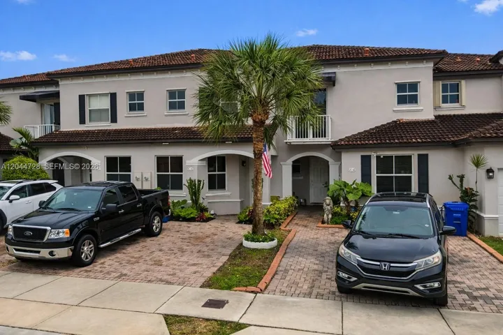 Two-story residence with a clean exterior and a lovely front entry. Features a tiled roof, white-framed windows, and a tropical garden with tall succulents and ornamental plants. Located in the desirable Century Gardens condominium.