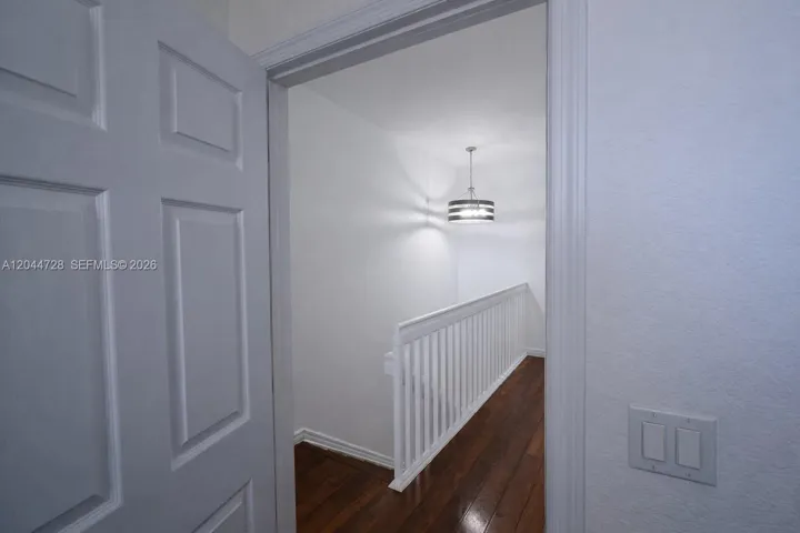 Clean hallway with white walls, laminated flooring, and modern light fixture. Features a sleek staircase and multiple doors for convenient access.