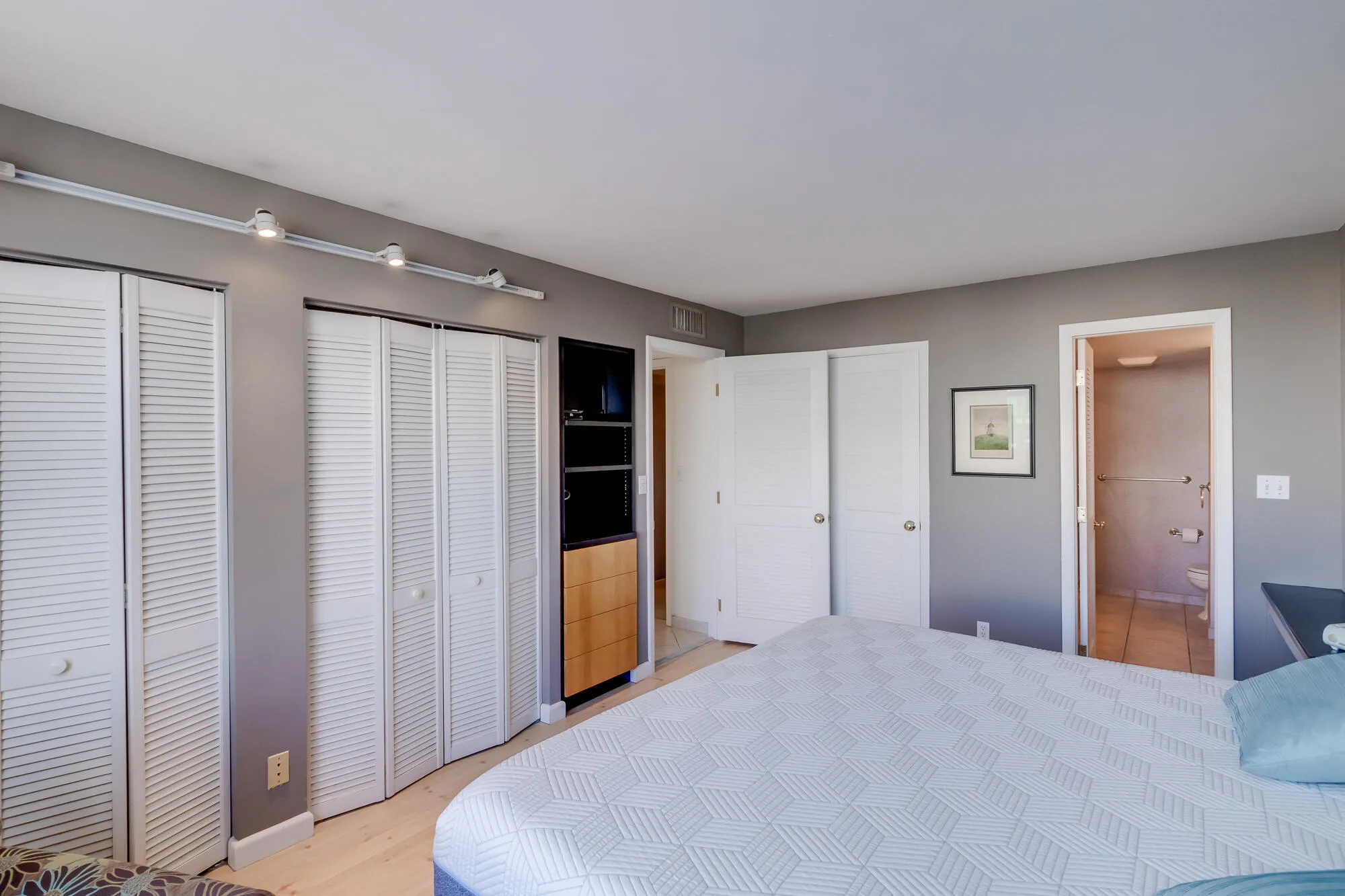 White louvered bi-fold doors, built-in shelving with wood-finish drawers, track lighting, and a neutral wall color