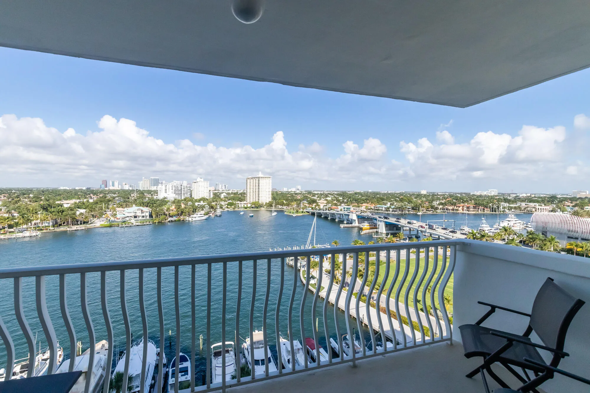 Balcony overlooking a waterway with boats, a distant bridge, and a city skyline