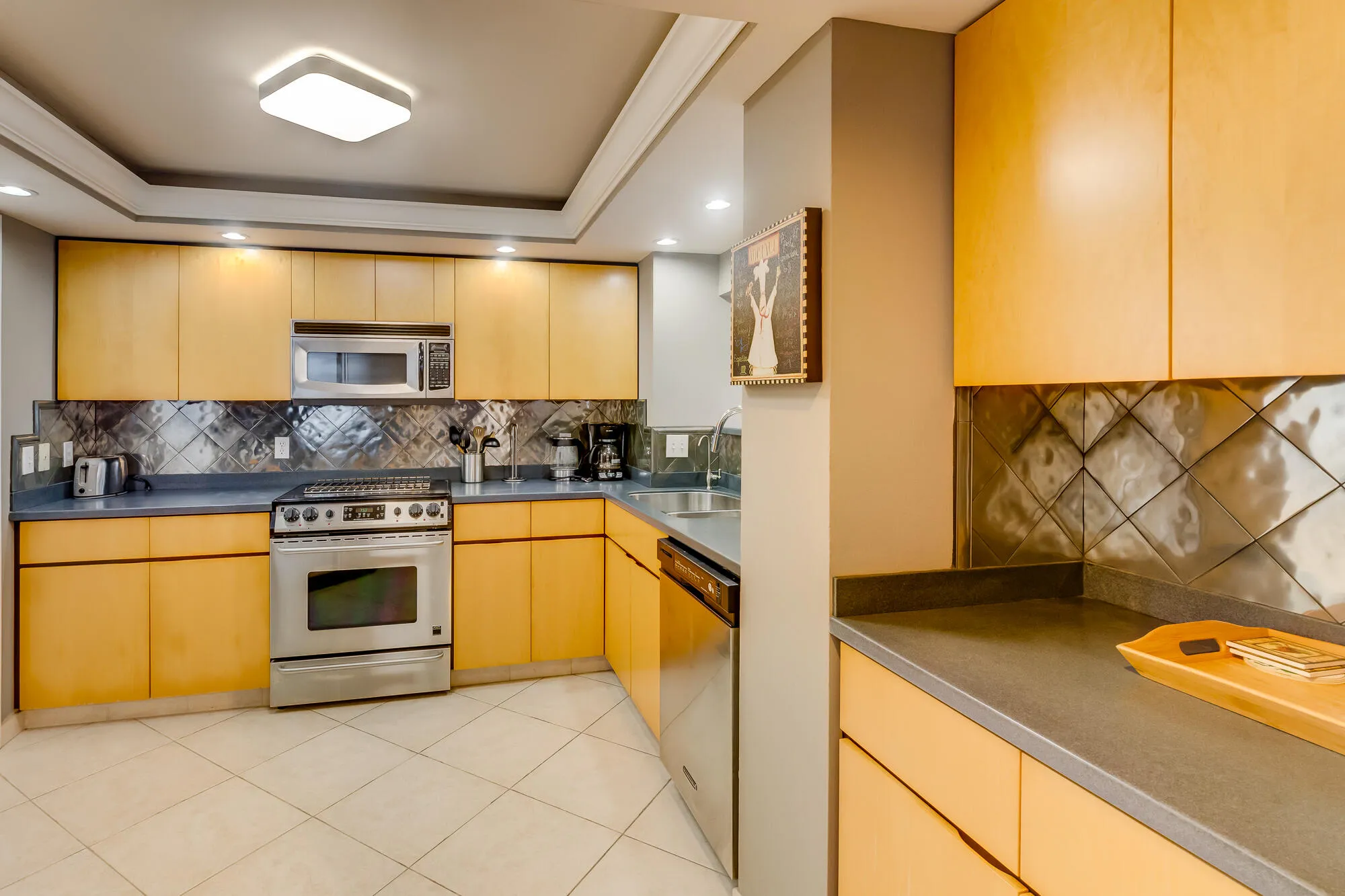 Modern kitchen featuring light wood cabinetry, stainless steel appliances, a unique textured backsplash, and recessed ceiling lighting