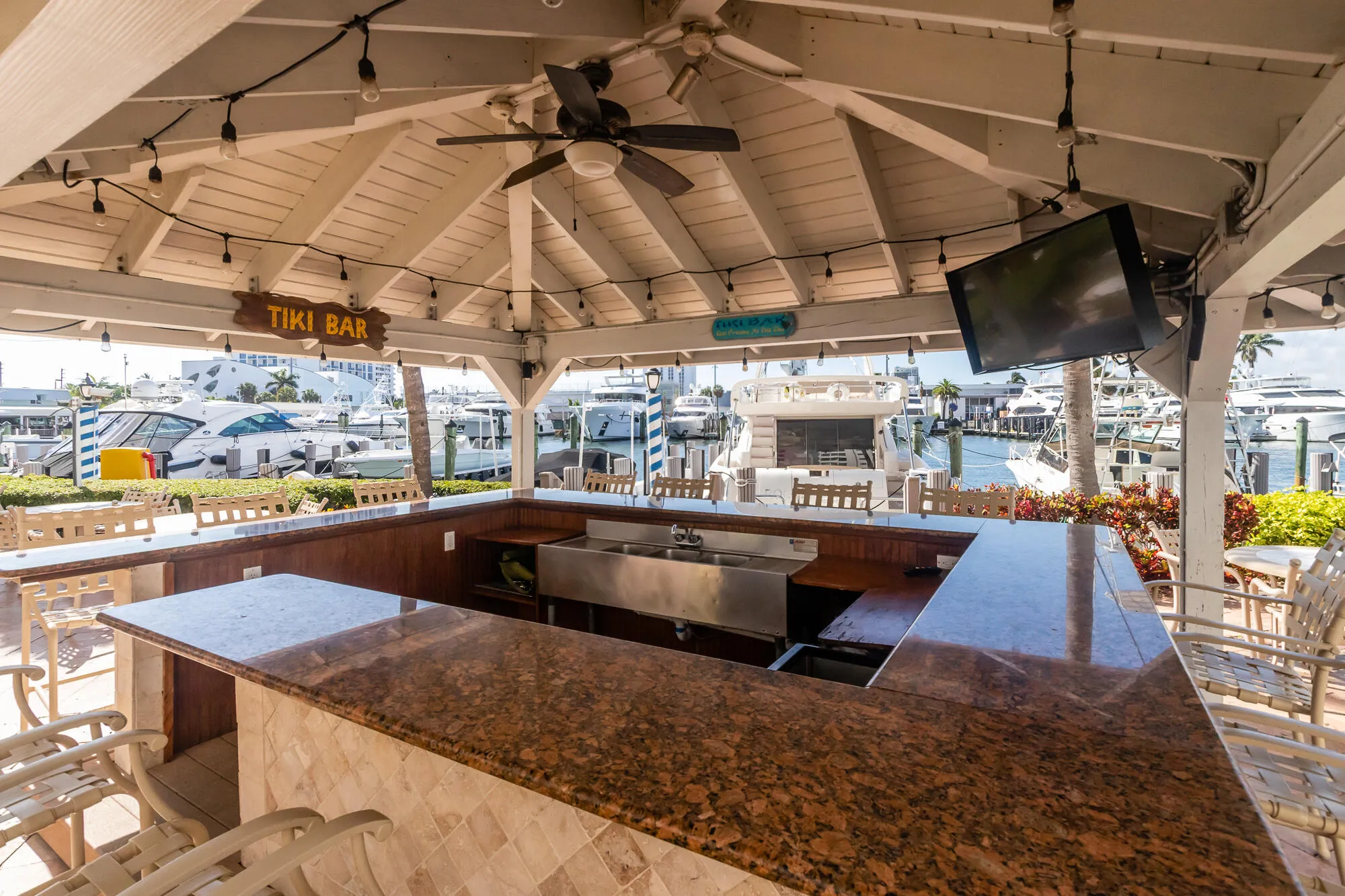 Covered outdoor bar with a natural stone countertop, built-in stainless steel sink, and exposed beam ceiling
