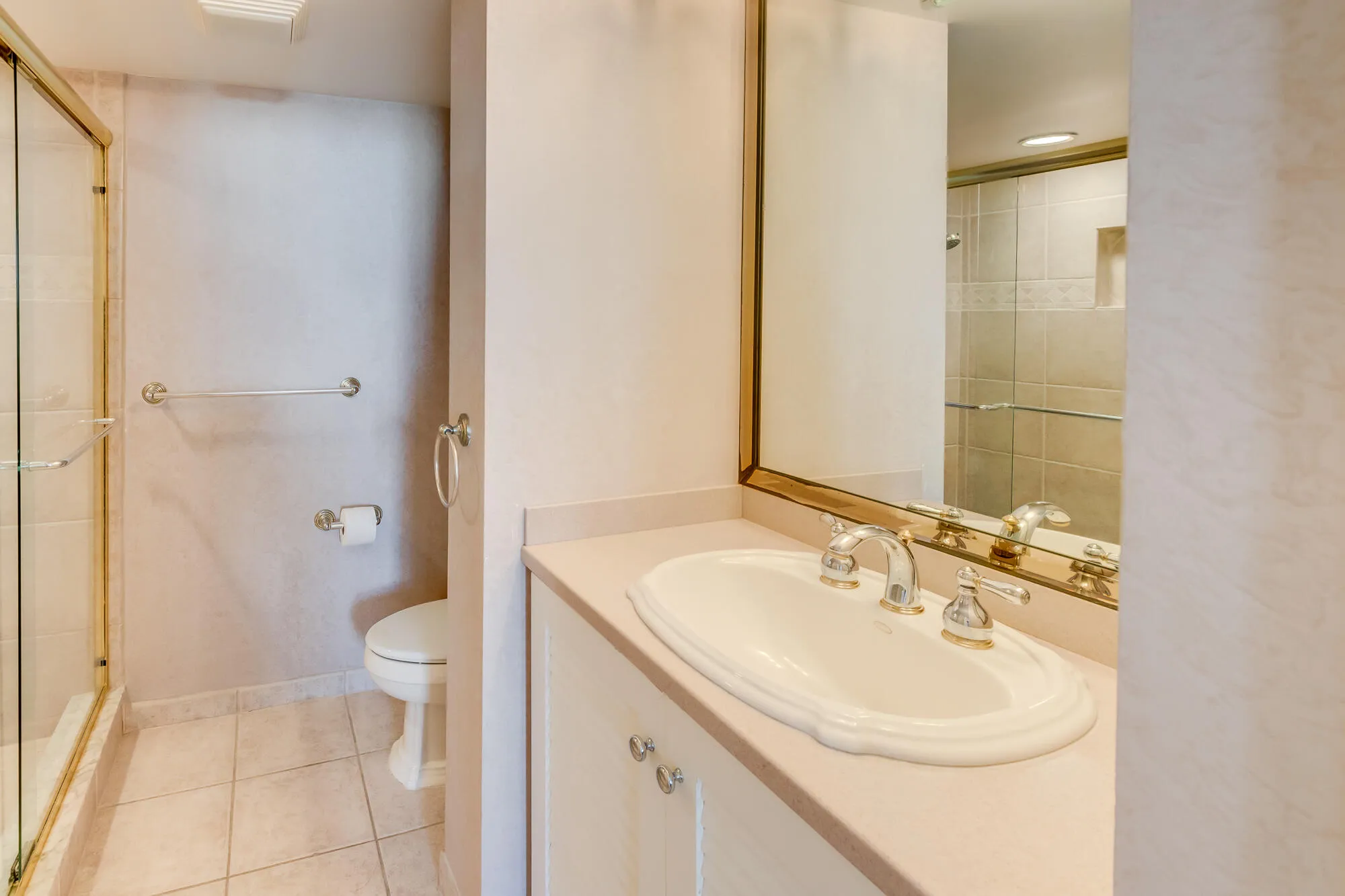 Vanity with integrated sink, polished chrome faucet, framed mirror, and glass-enclosed shower with tiled walls