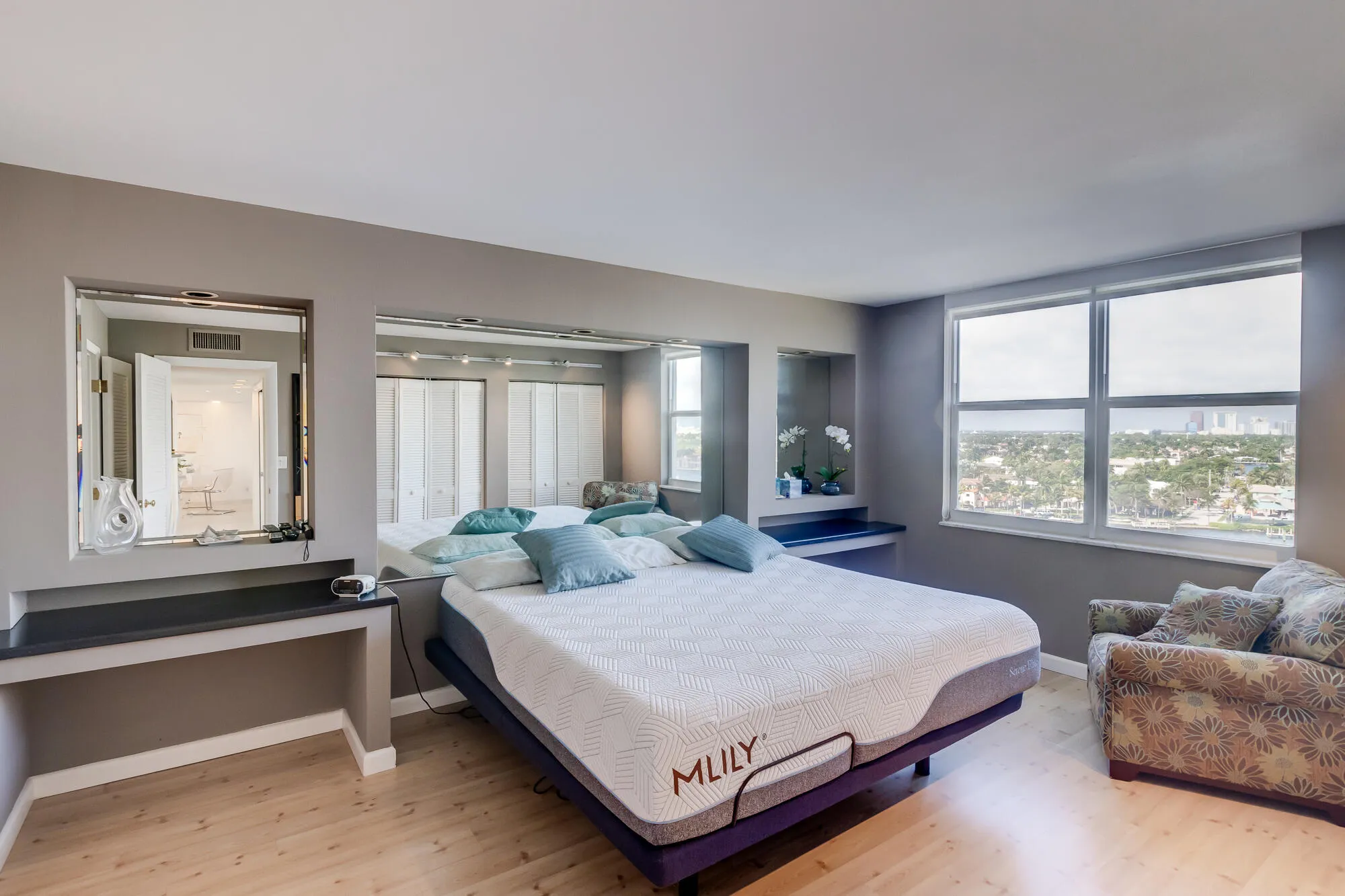 Recessed built-in vanity area with mirror, full-wall mirrored accents, built-in shelving, wood-finish flooring, and large windows