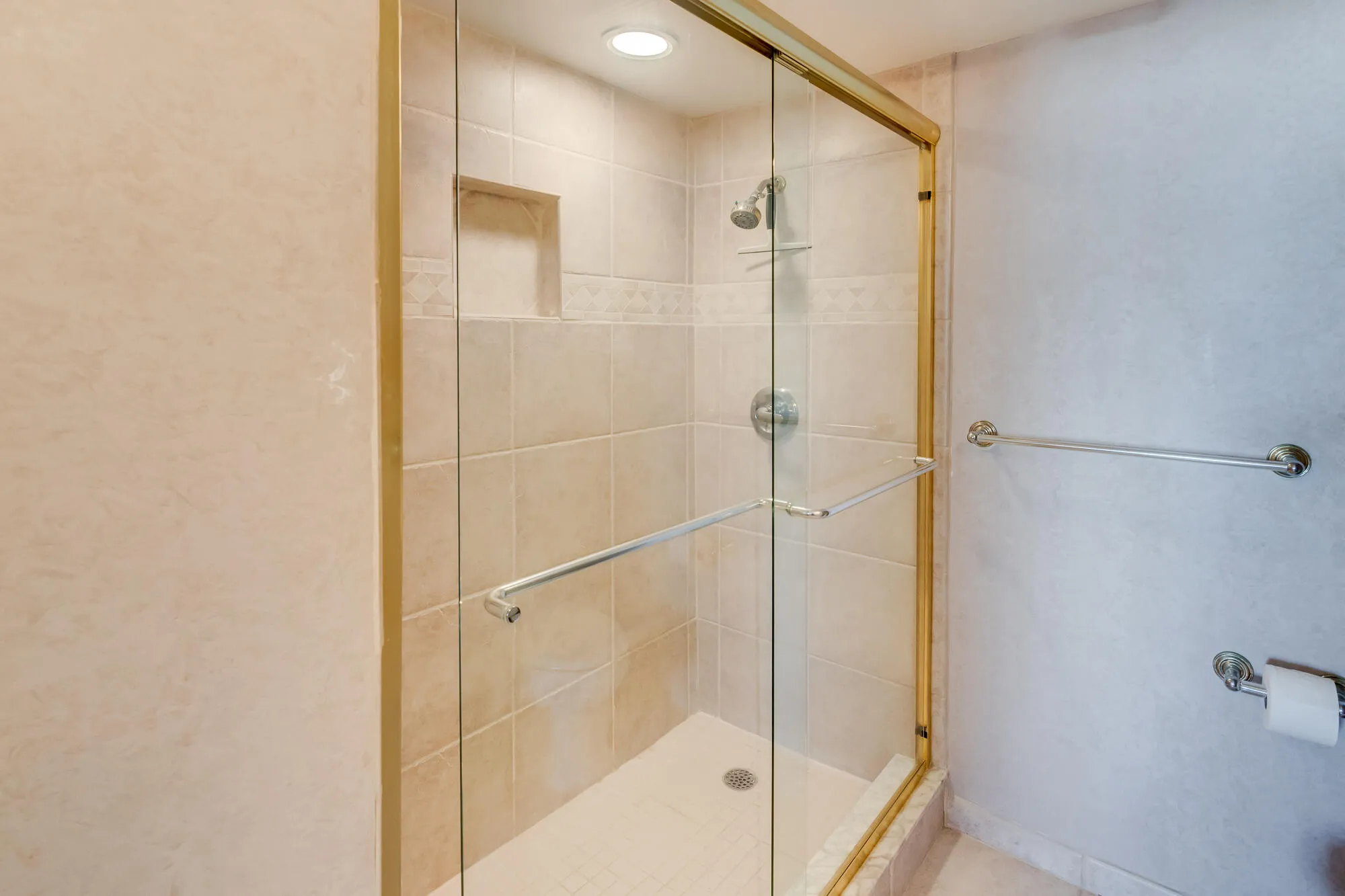 Glass-enclosed shower with gold-tone framing, tiled walls, built-in shower niche, and a recessed ceiling light