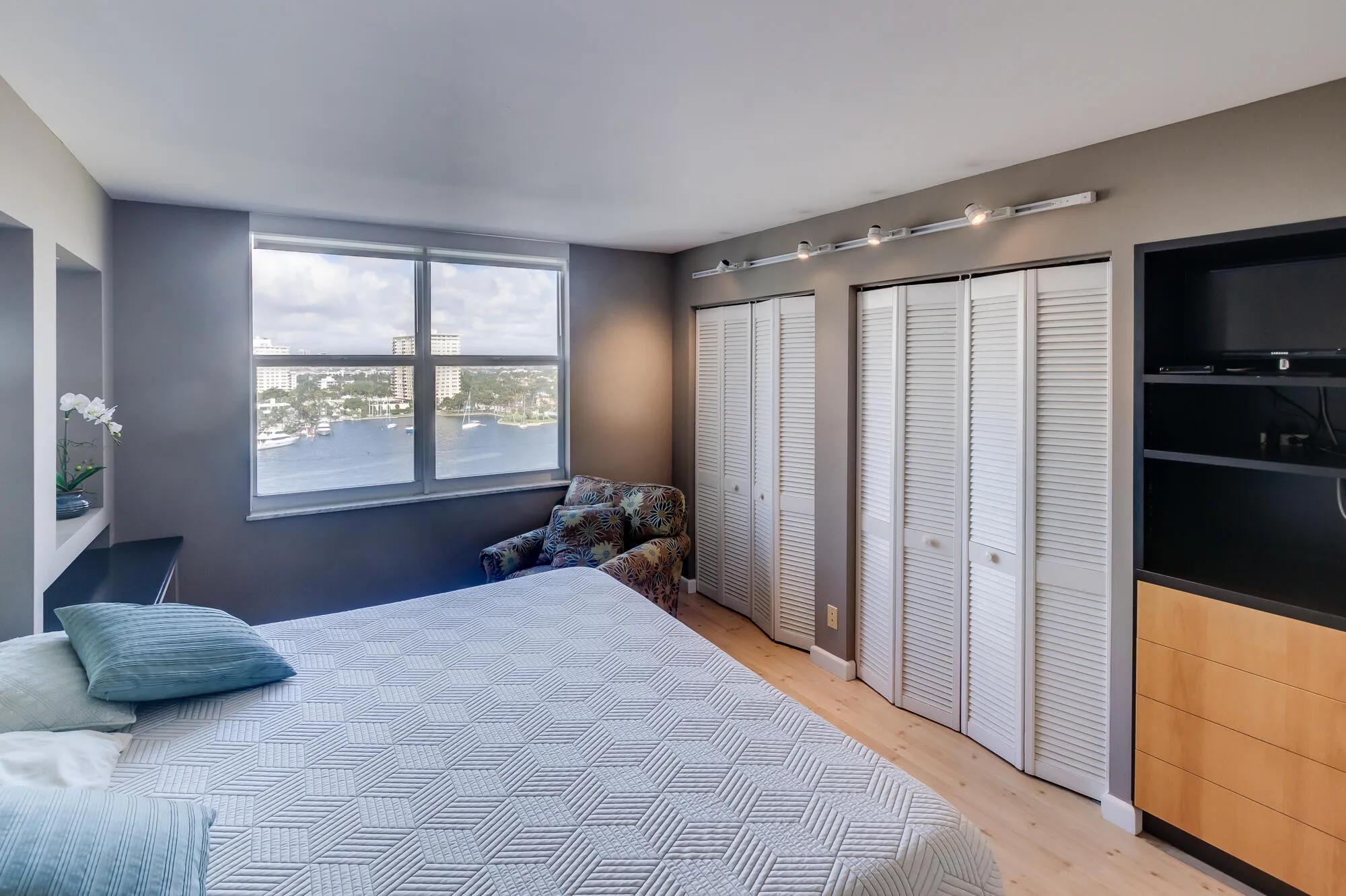 Large window with a water and city backdrop, two built-in storage alcoves, two louvered bifold closet doors, built-in shelving with integrated drawers, and wood-finish flooring