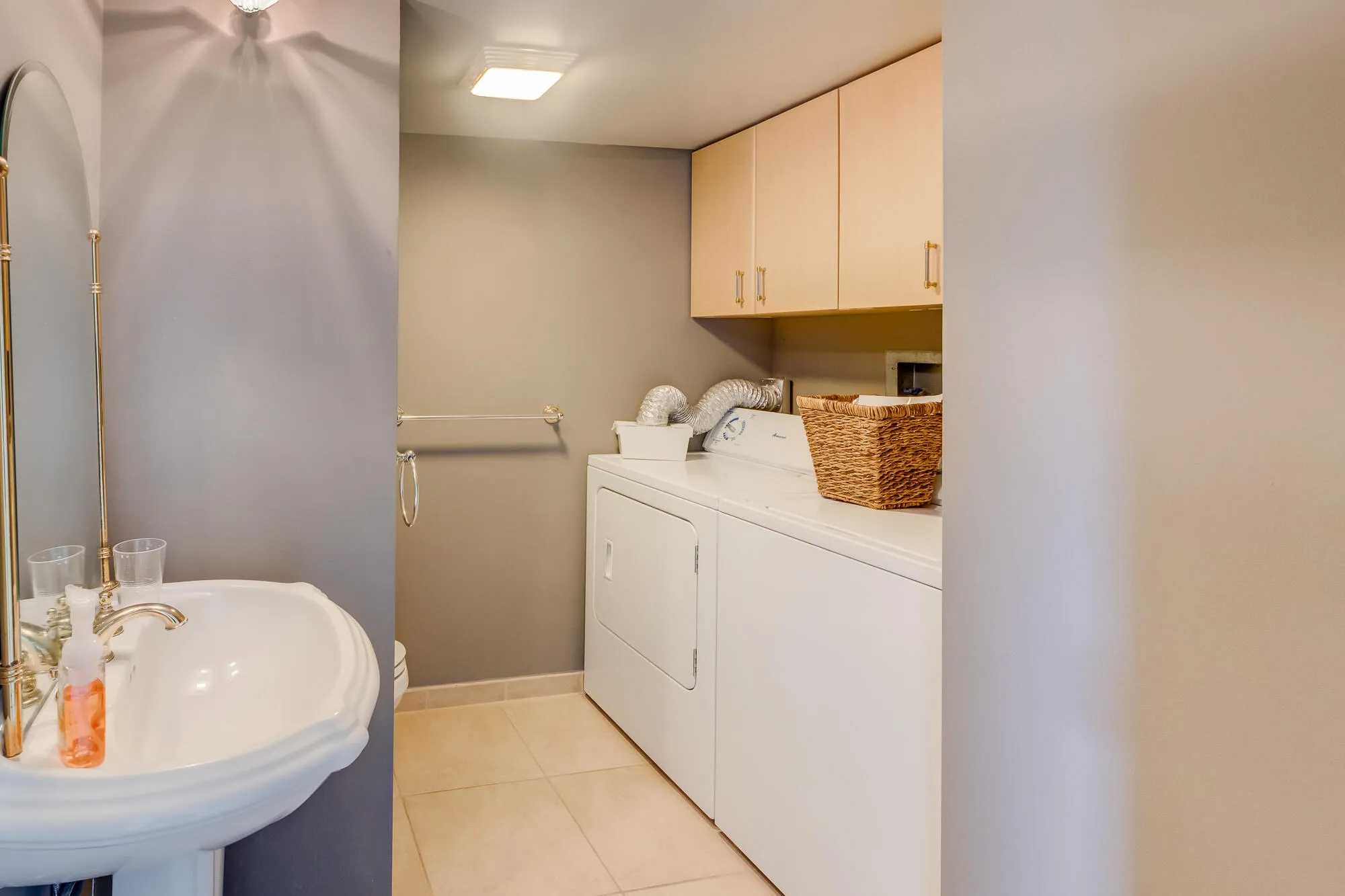 Pedestal sink with brass-finish faucet, overhead lighting, neutral wall paint, built-in upper cabinetry, and tile flooring