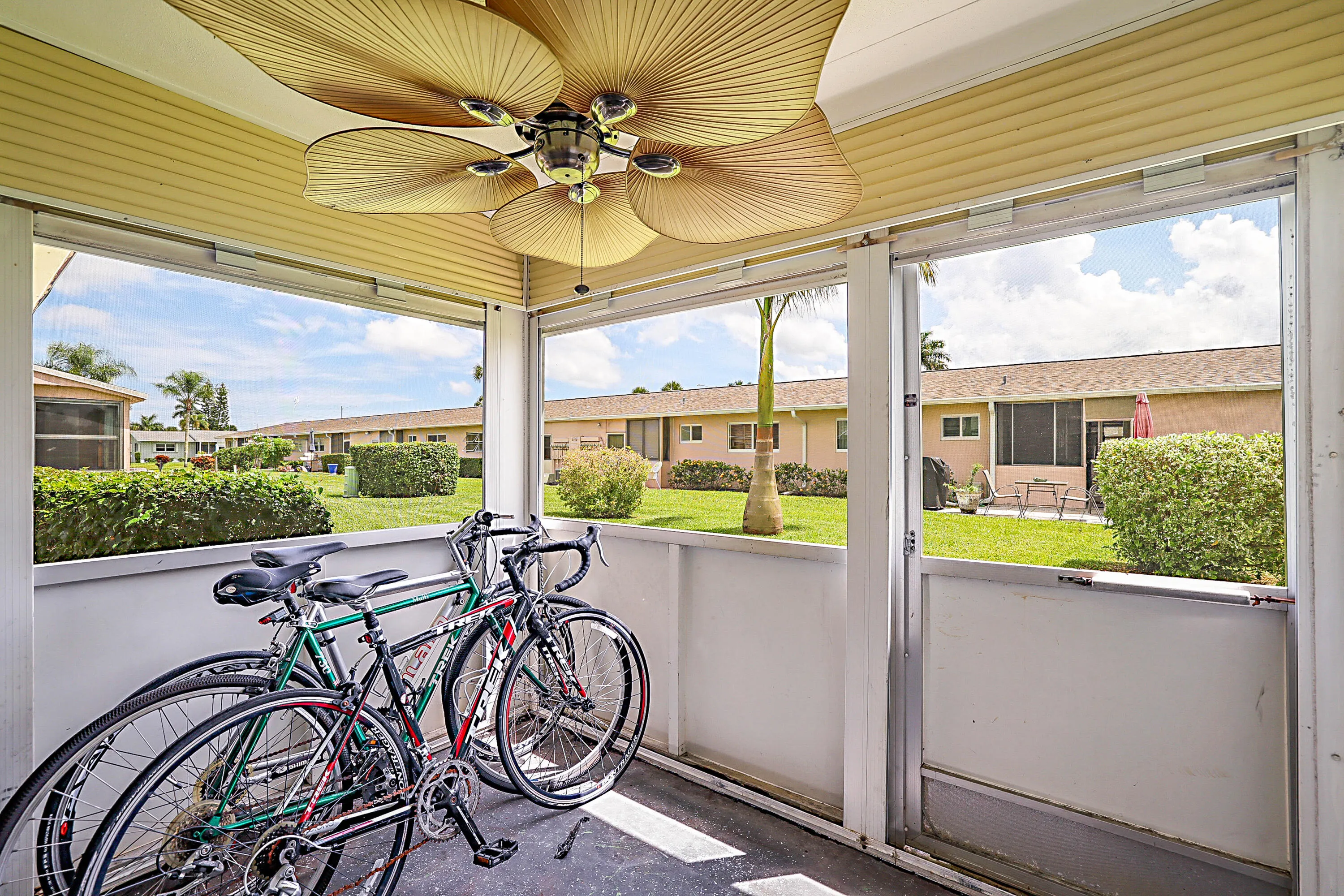Screened porch featuring a ceiling fan with palm-leaf style blades, exterior siding, and a landscaped outdoor area
